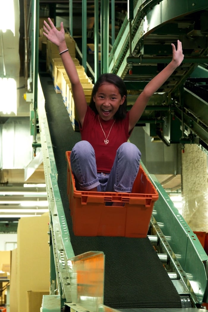 Doctored image of a child riding on the warehouse conveyor belt like a roller coaster during Bring Your Child To Work Day